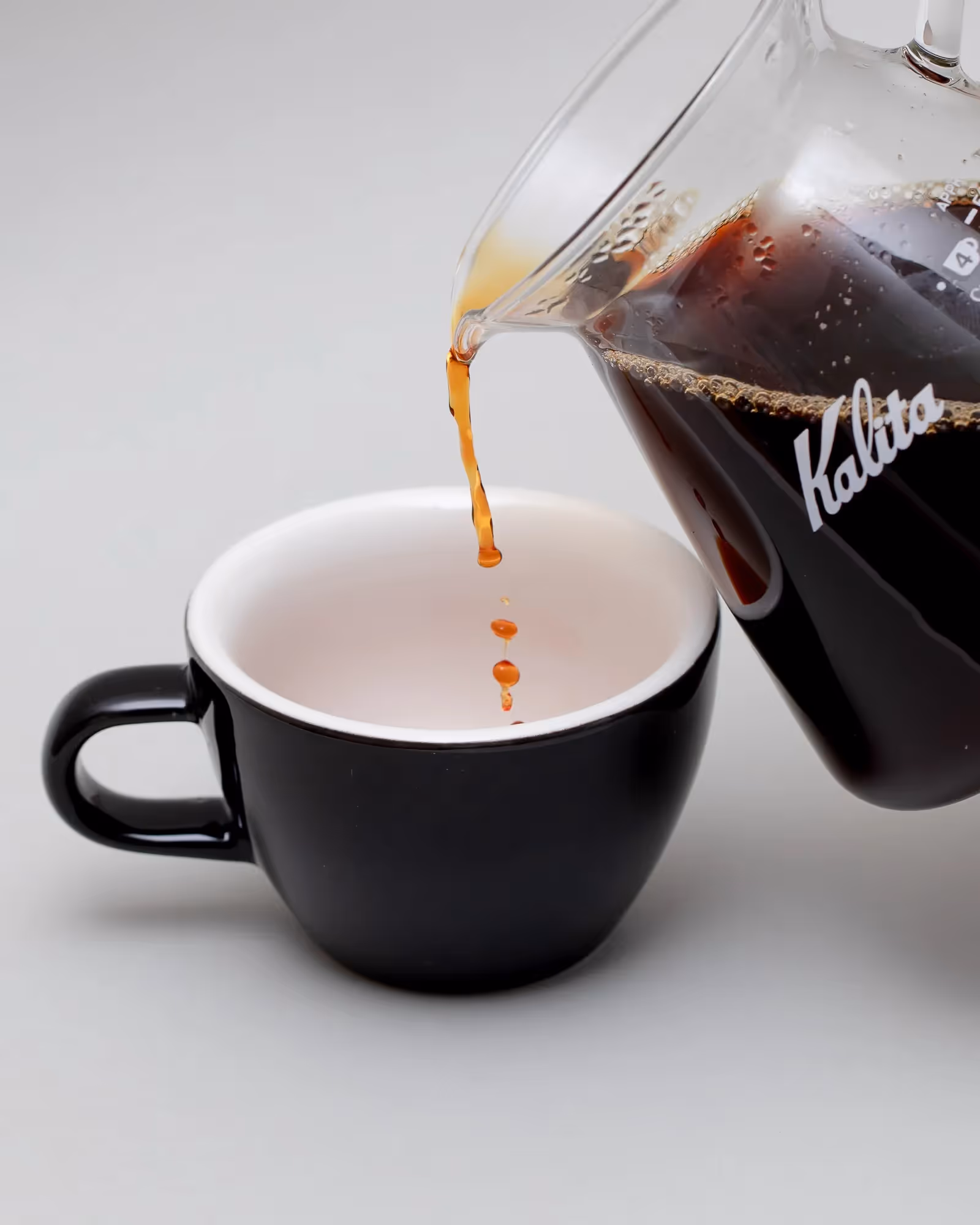 Pouring filter coffee from Kalita jug into black cups