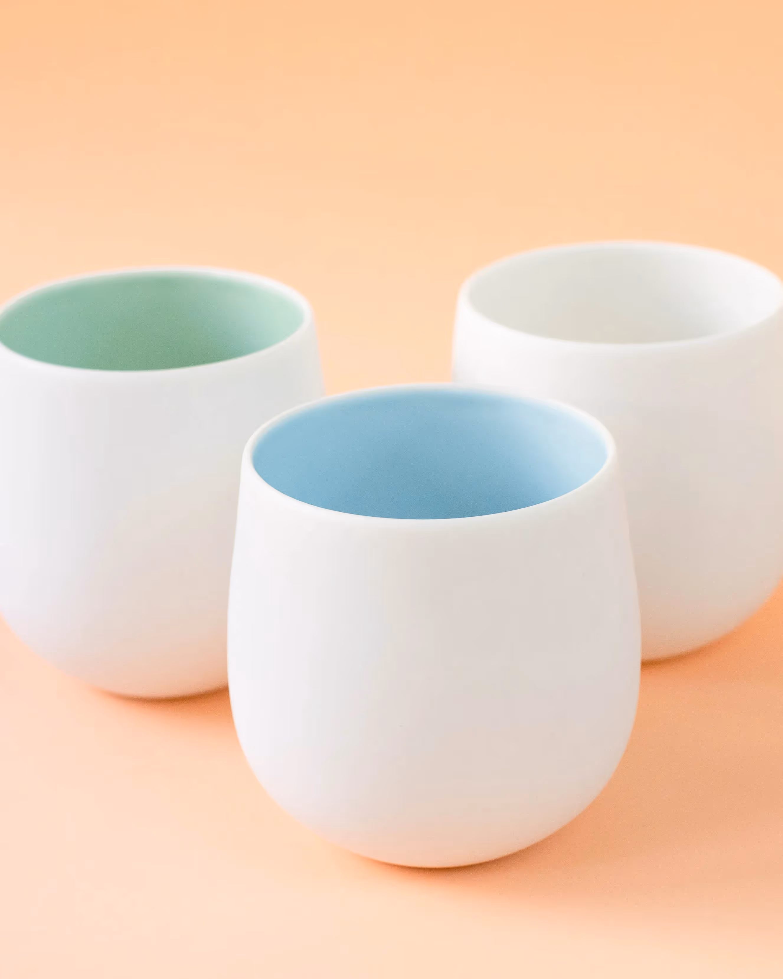 Three minimalist round ceramic coffee cups on a pastel orange background