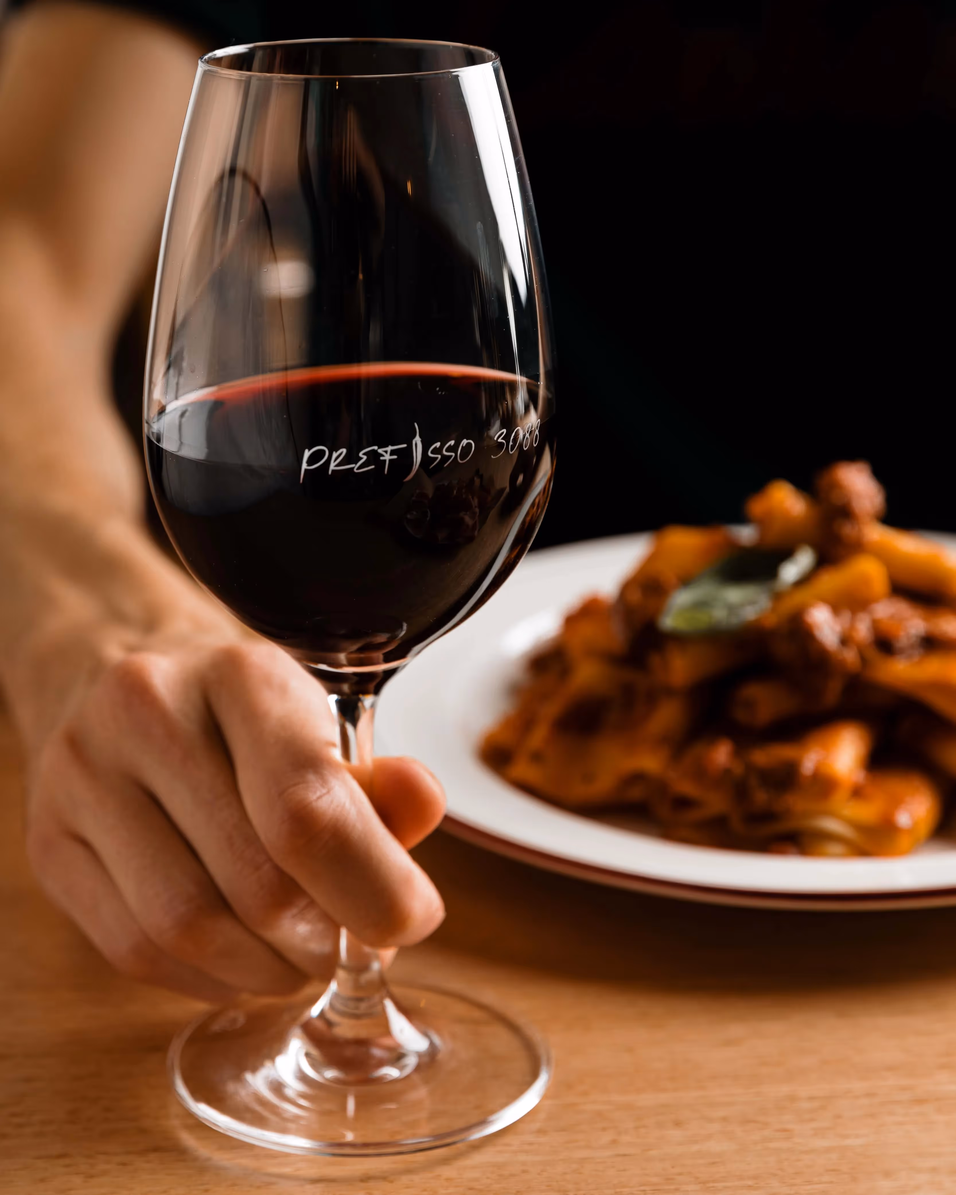 Wine glass featuring Preffiso 3088 logo staged in front of pasta dish