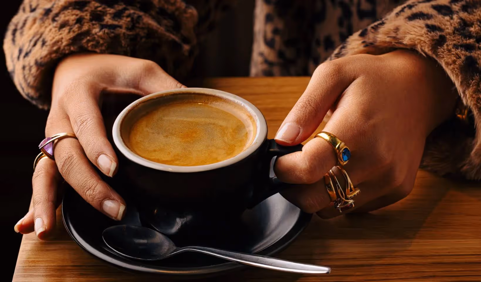 Elegant woman with rings on fingers holding a cappuccino