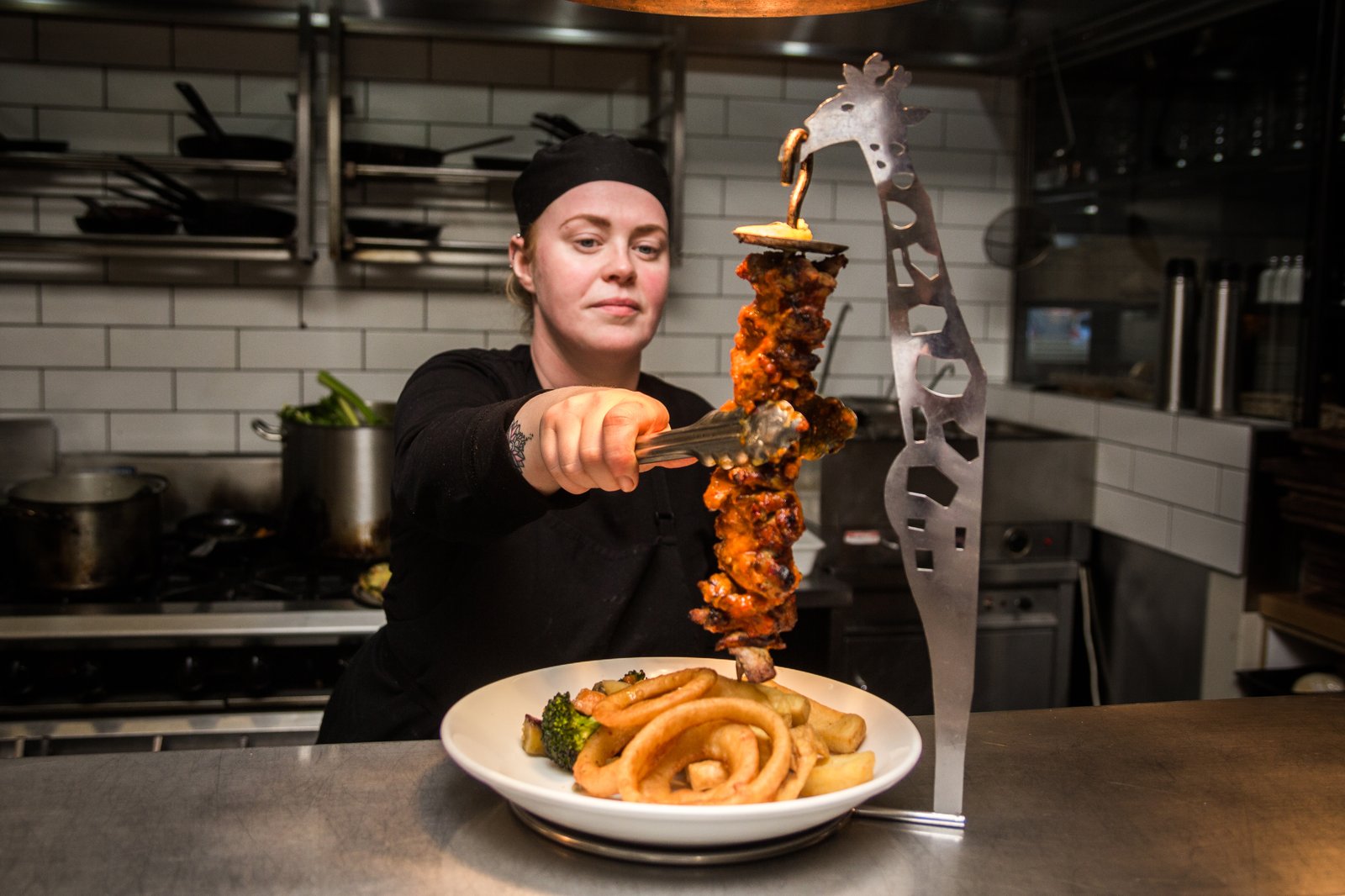 Chef assembling a tall skewer over a plate of chips