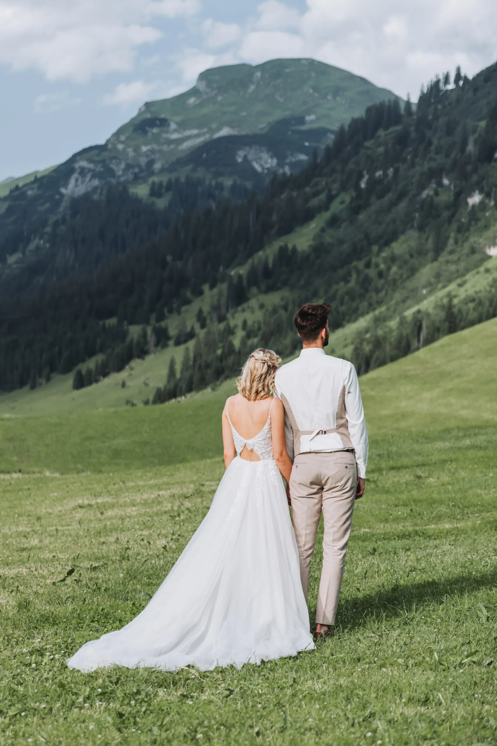 Brautpaar steht Hand in Hand auf einer Wiese mit Blick auf die Berge