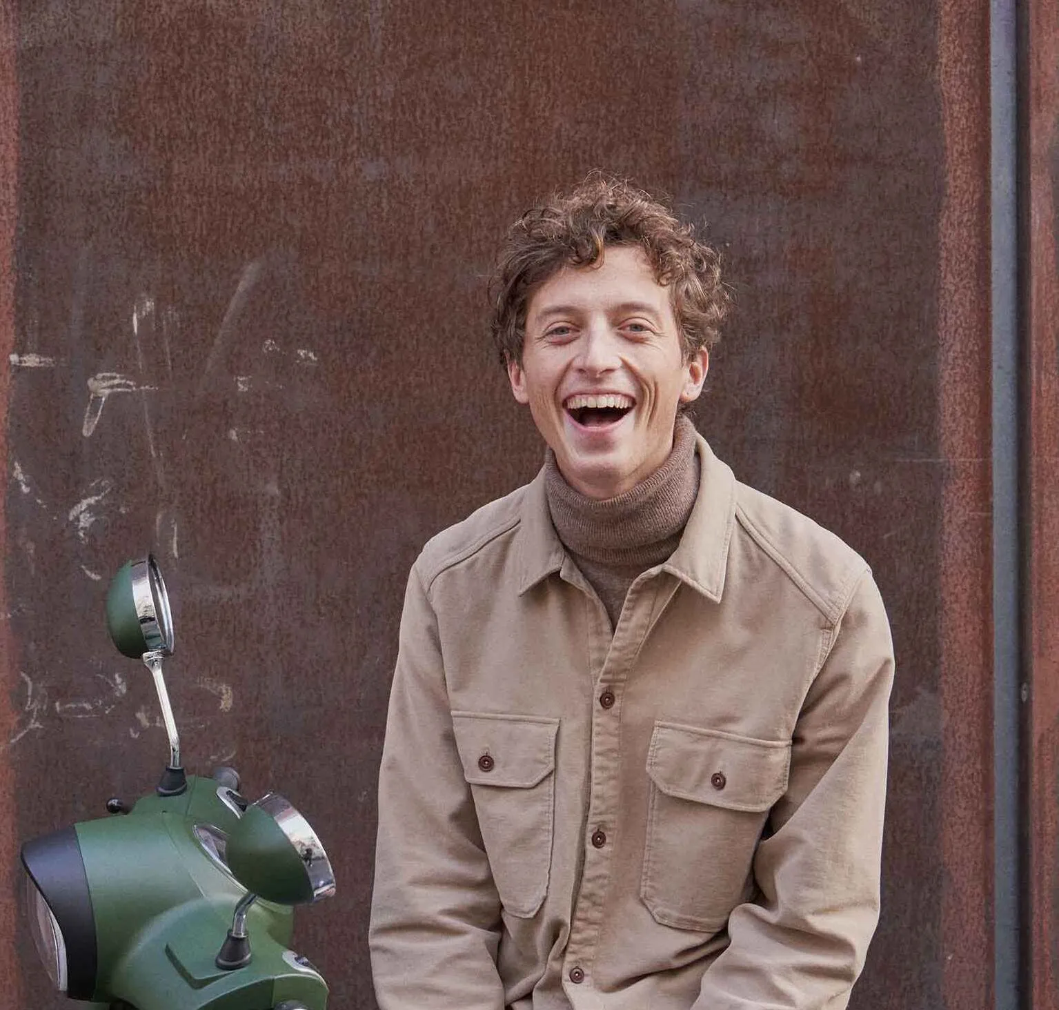 Un jeune homme rit assis sur un scooter