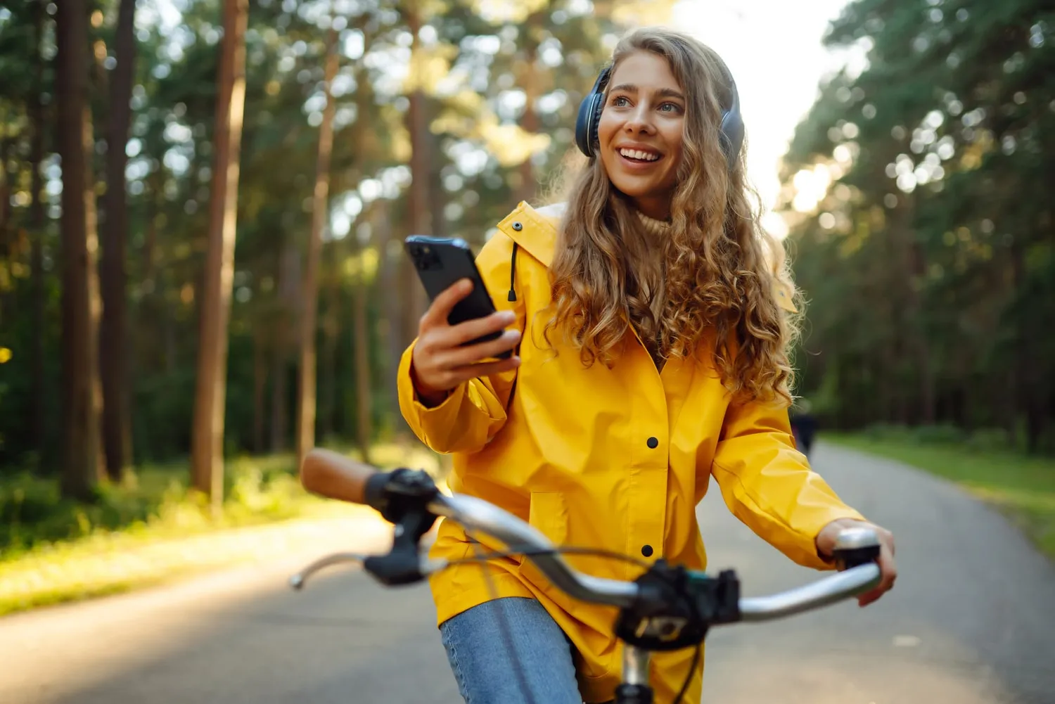 Une femme en vélo, se balade en forêt avec son téléphone dans la main