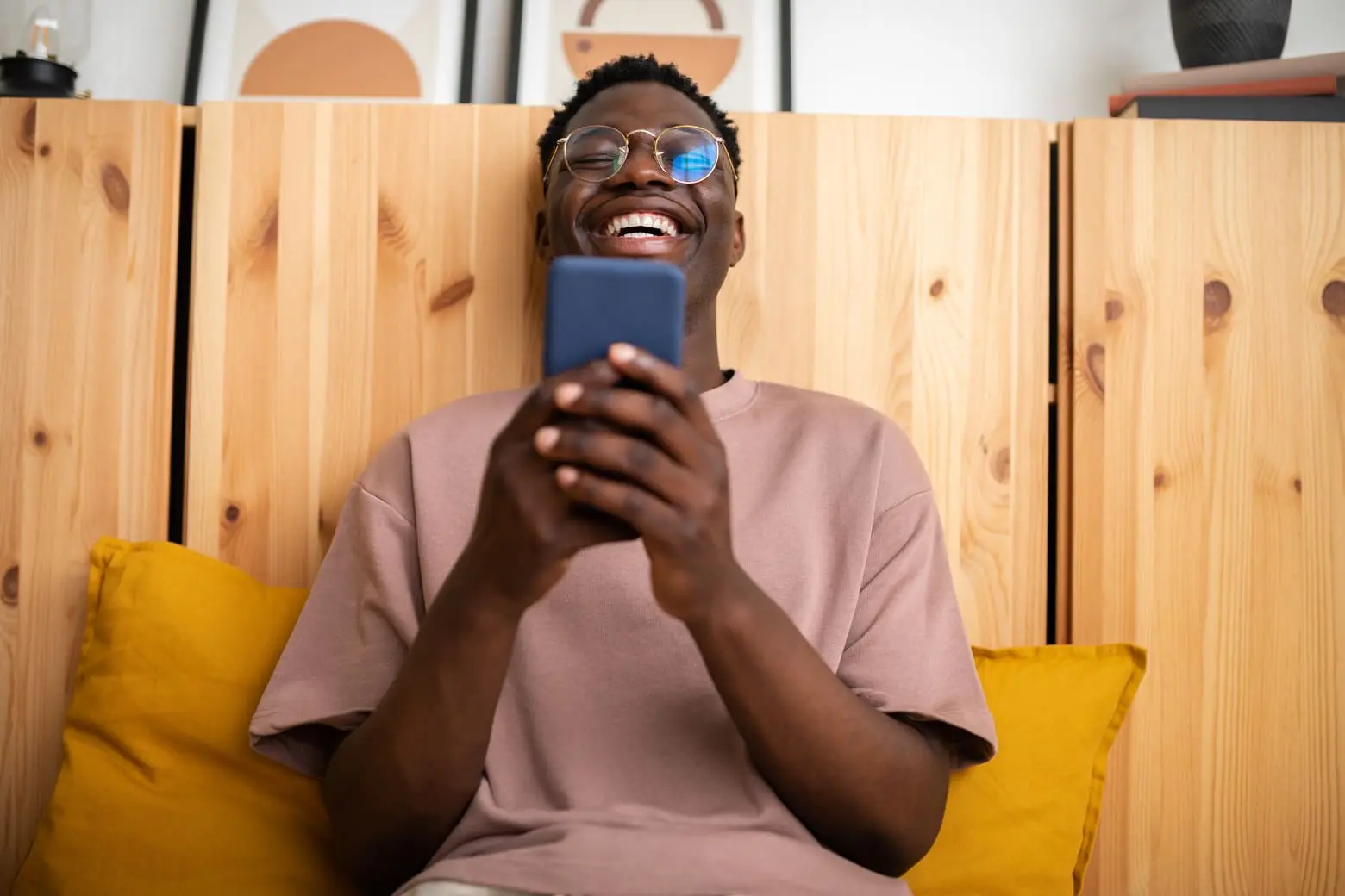 Homme à lunettes souriant, tenant un téléphone dans ses mains