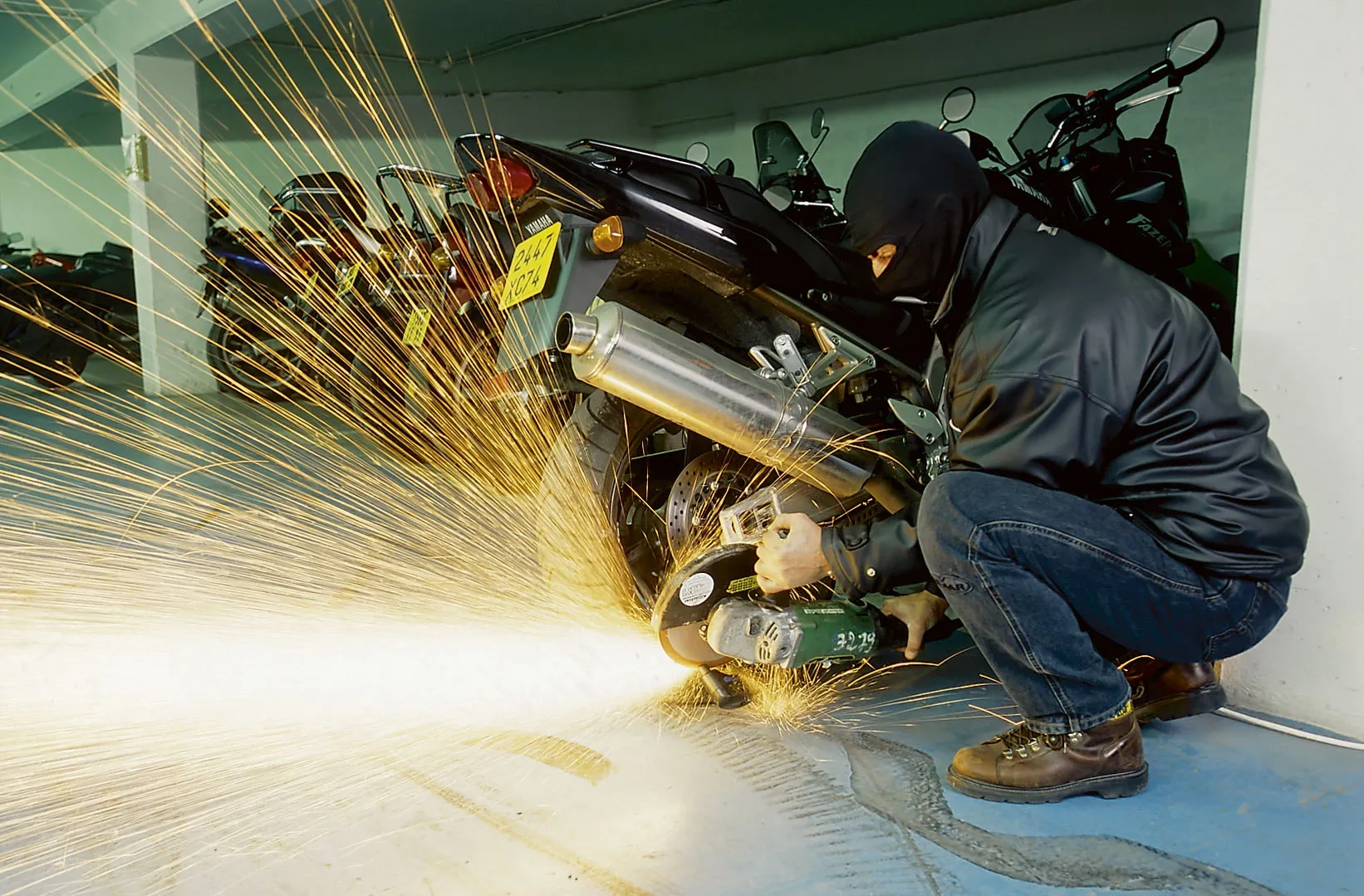 un homme cagoulé scie l'antivol d'une moto