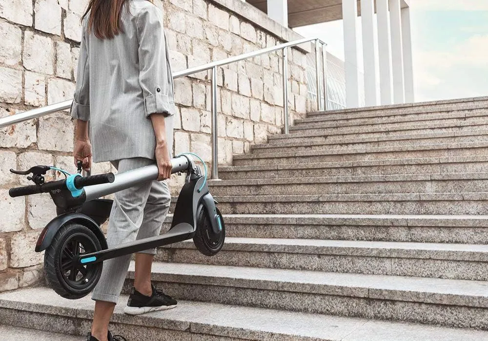 Une femme qui monte les escaliers avec sa trottinette électrique pliée dans les mains