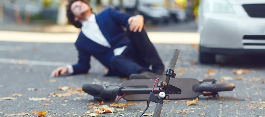 Un homme qui tombe sur le sol en tenant son genou avec sa trottinette électrique devant lui