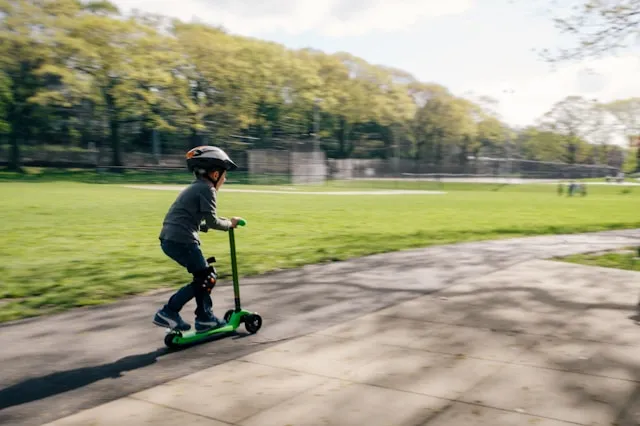 Un enfant avec un casque sur un trottinette dans un parc