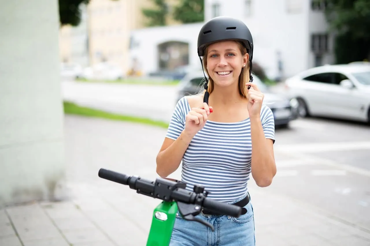 Une femme qui monte sur une trottinette électrique et qui enfile son casque