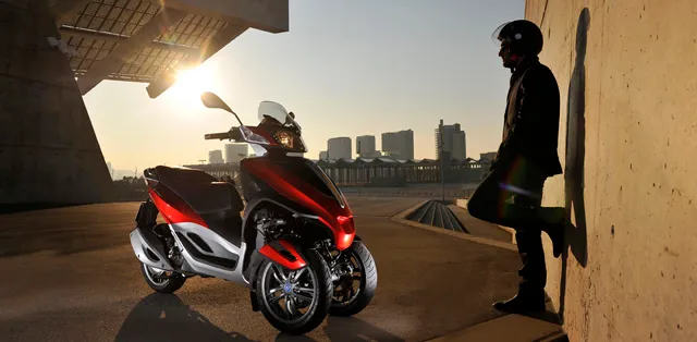 Scooter à trois roues garé à côté d'un homme debout contre un mur