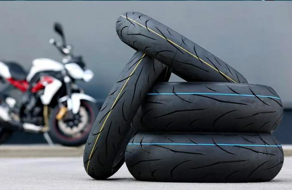 Différents modèles de pneus de moto empilés les uns sur les autres avec une moto en arrière plan