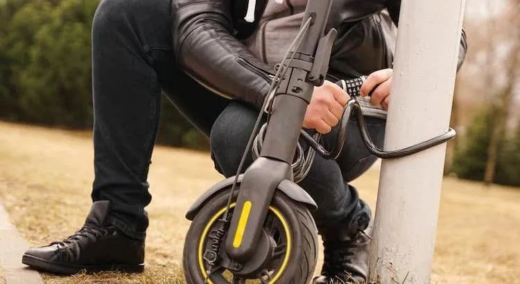 Un homme qui tente d'enlever les attaches d'une trottinette électrique fixé sur un pilier en métal.