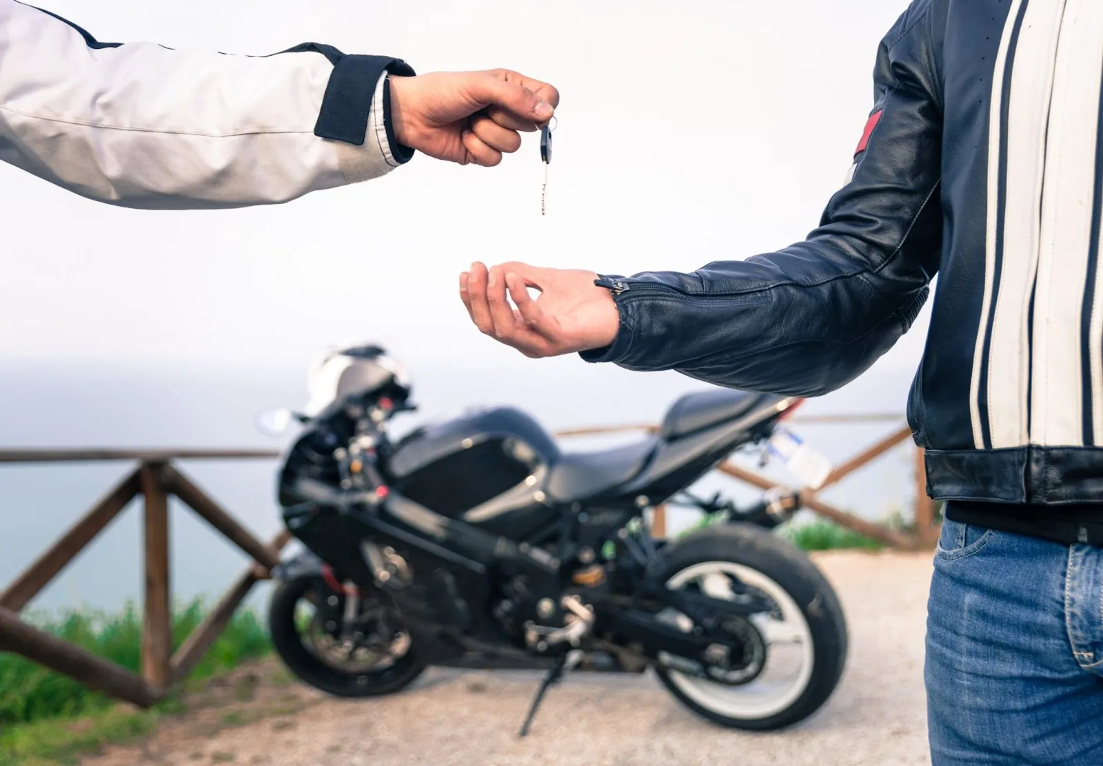 Un homme qui passe une clé à un autre avec une moto à l'arrière. 