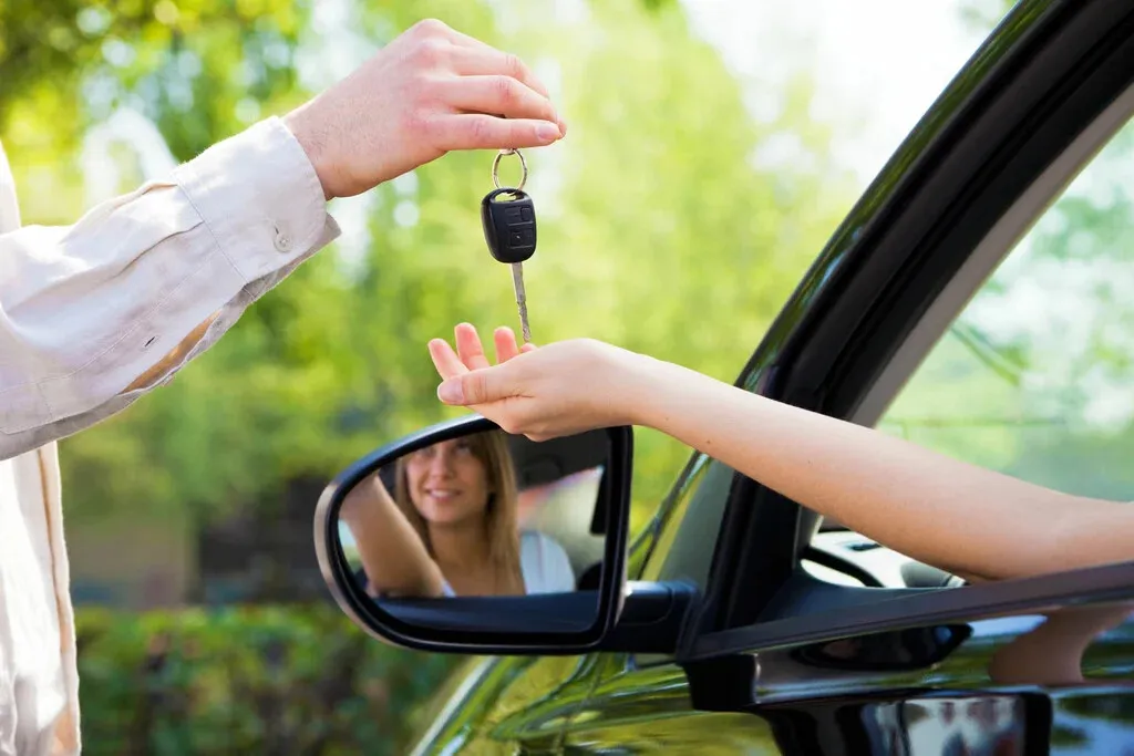 Une femme qui tend la main en dehors d'une voiture pour prendre la clé que lui tend une autre personne.