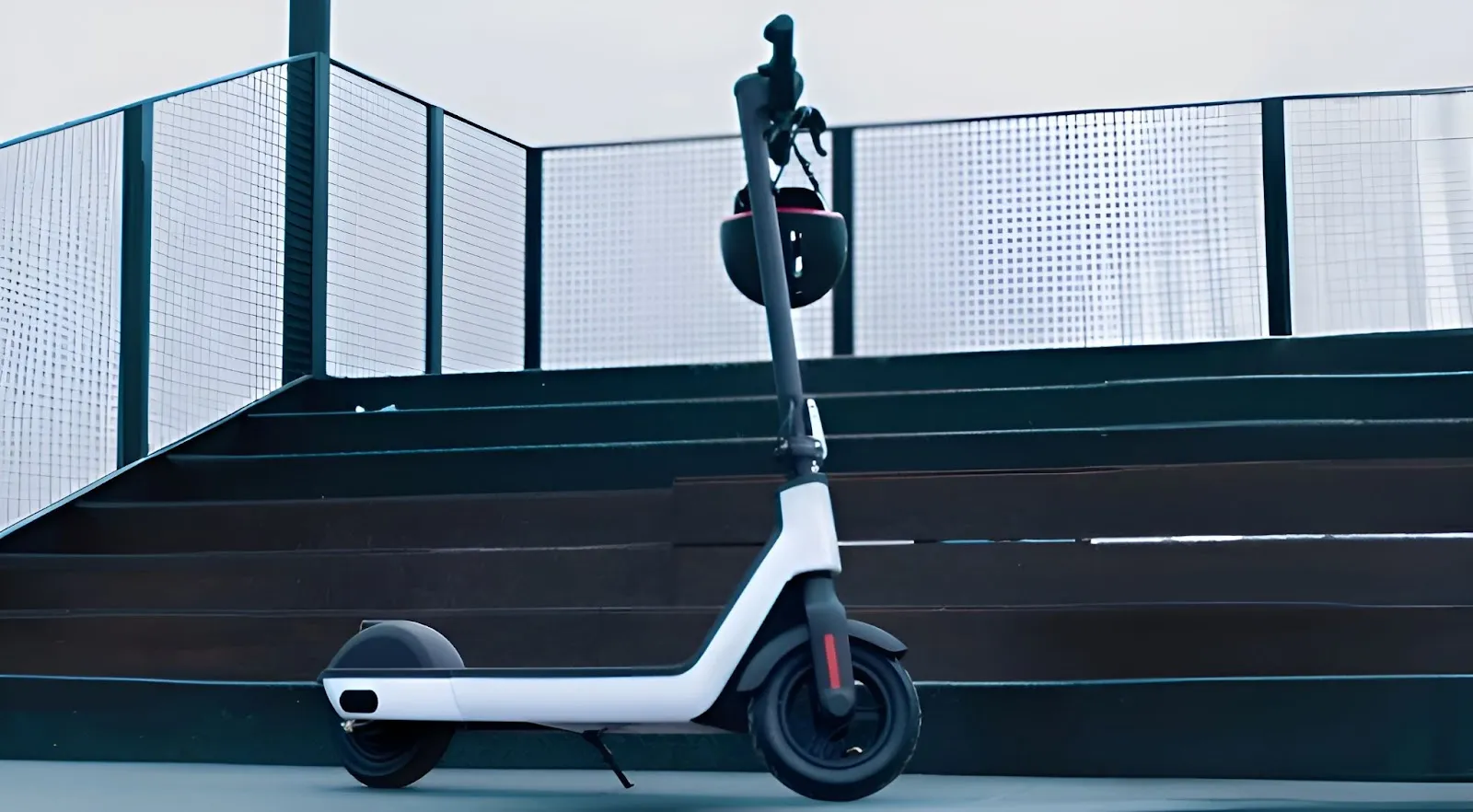 Une trottinette électrique garée devant un escalier avec un casque sur le guidon.