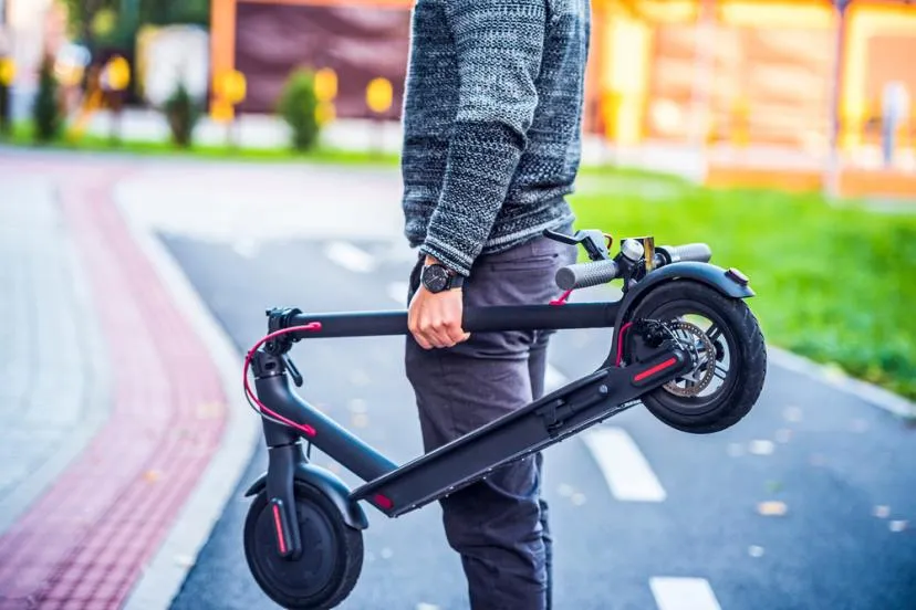 Un homme qui tient une trottinette électrique pliée dans sa main dans la rue.