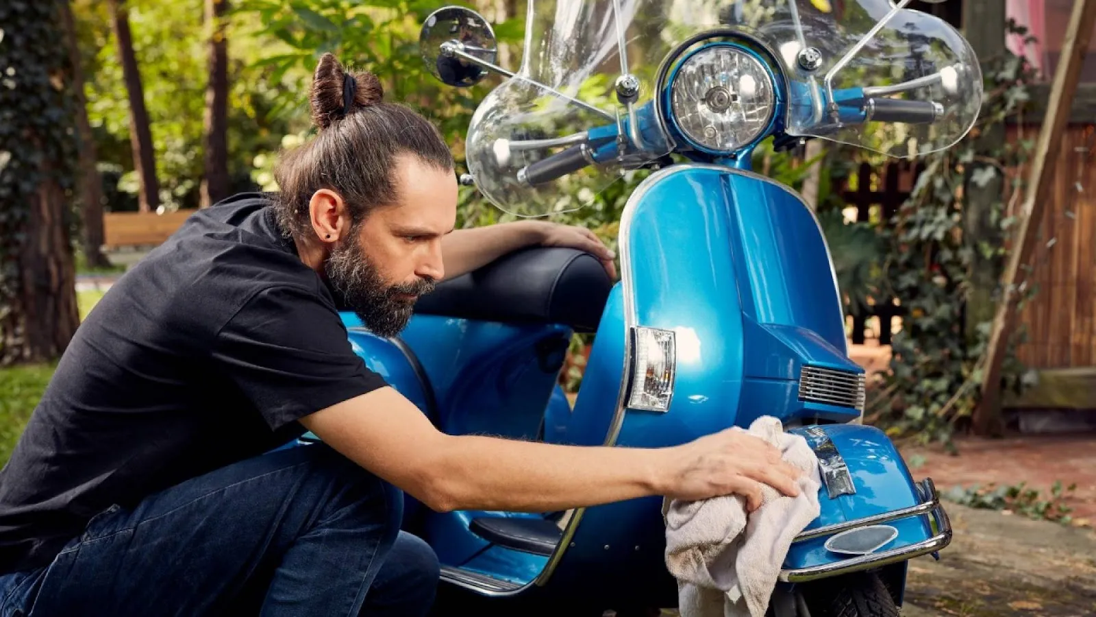 Un homme en train de nettoyer son scooter bleu avec un chiffon. 