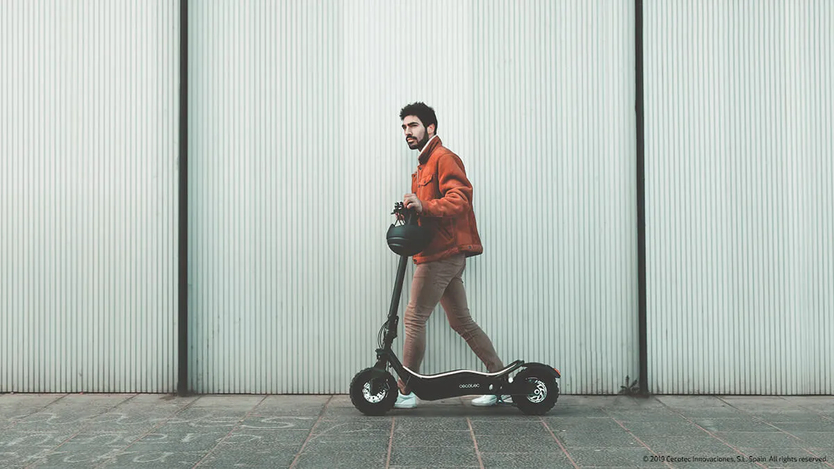 Un homme qui marche avec sa trottinette électrique Cecotec Bongo Z+ Offroad dans la rue