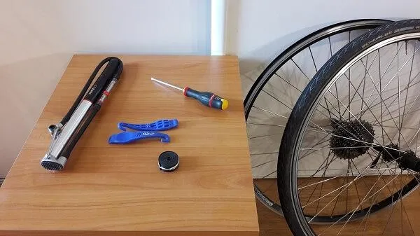 Un pneu et une jante posés à côté d'une table sur laquelle est posée une pompe, un démonte-bleu et un tournevis.