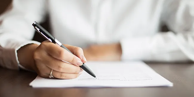 Un homme écrit sur une feuille de papier avec un stylo.