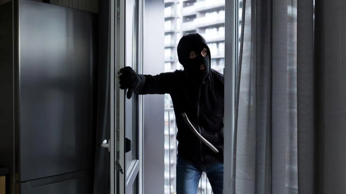 Un homme masqué avec un pied de biche qui pénètre dans une maison.