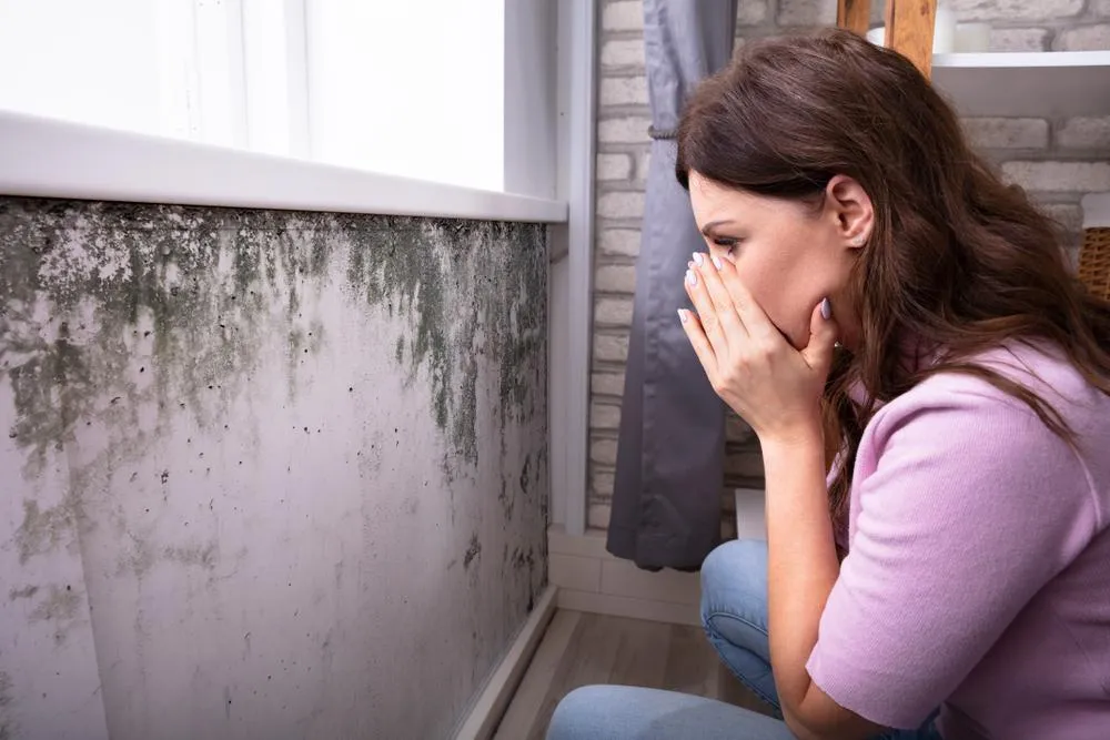 Une femme qui regarde un mur touché par l'humidité et qui se tient la bouche.