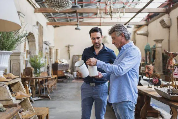 Un homme qui discute avec un autre au milieu d'un magasin d'accessoire de déco en tenant des pots blancs dans les mains. 