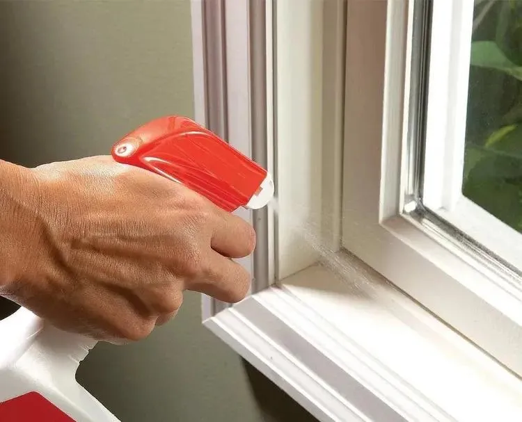 Une main qui tient un pulvérisateur et qui l'actionne près d'une fenêtre.