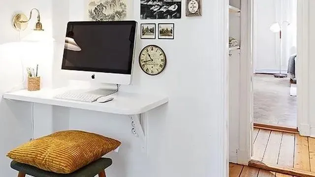 Un ordinateur posé sur une étagère blanche fixée contre un mur à côté de quelques décorations murales et une lampe de bureau.