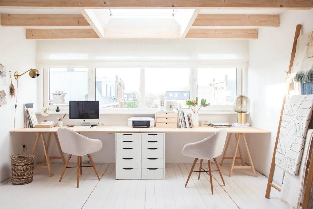 Une table de bureau qui est placée contre un mur avec des tiroirs de rangement sur la table et au milieu entre deux chaises. 