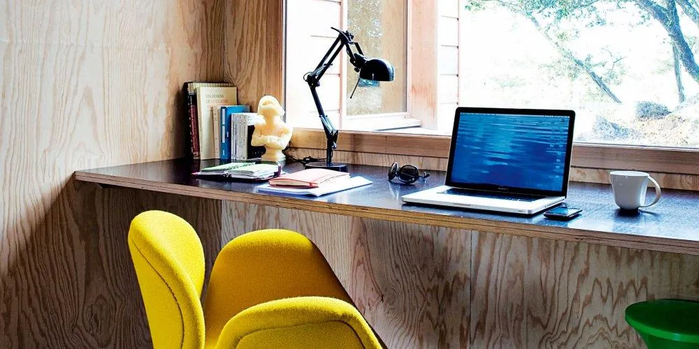 Un ordinateur posé sur une table de bureau à côté d'un Smartphone et d'une lampe de bureau, de quelques livres et une tasse blanche.