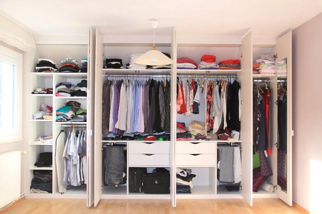 Un dressing avec des portes battantes ouvertes. Il est placé contre les murs qui est rangé.