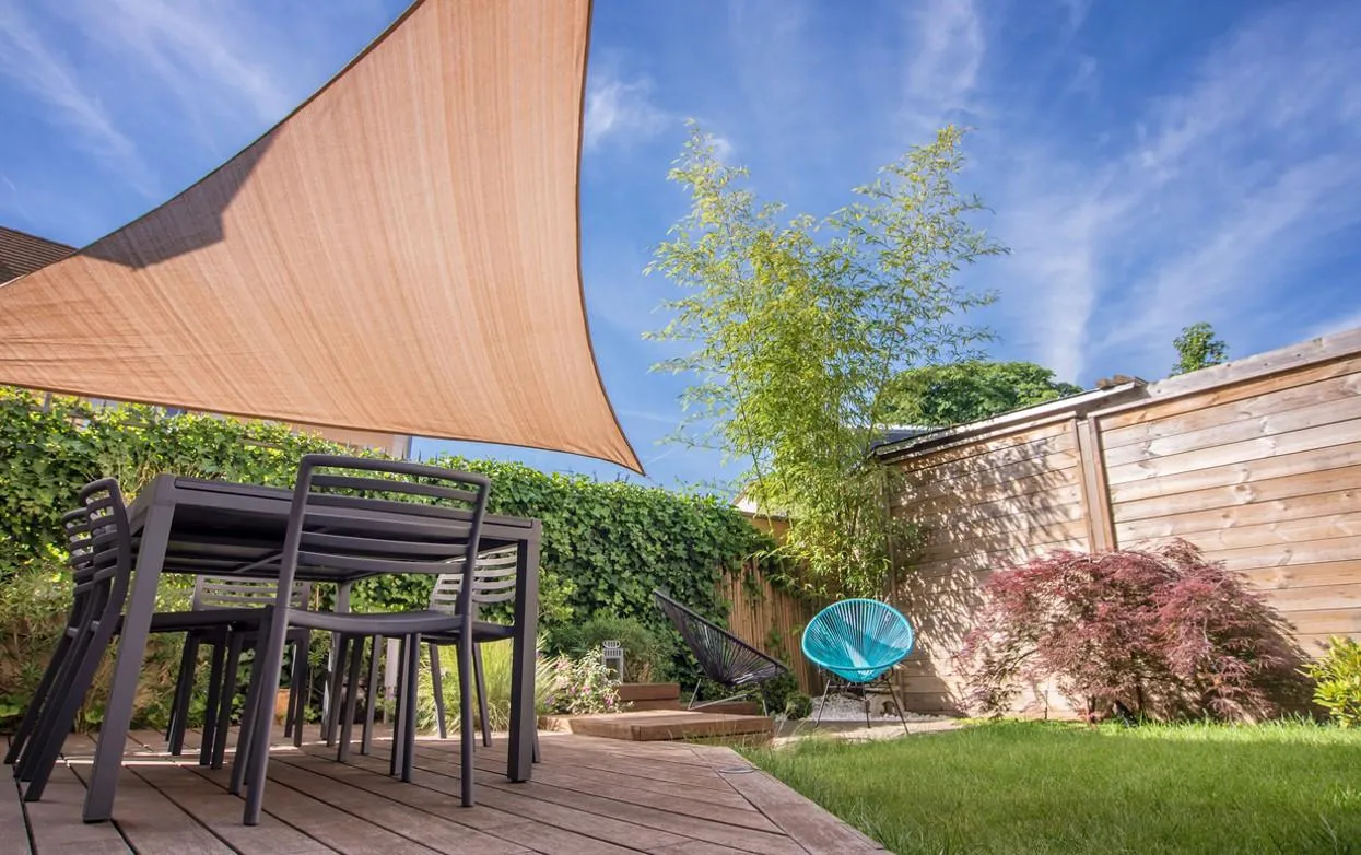 Une terrasse en extérieur couverte par une voile d'ombrage et décorée avec une table et des chaises de salle de à manger de jardin.