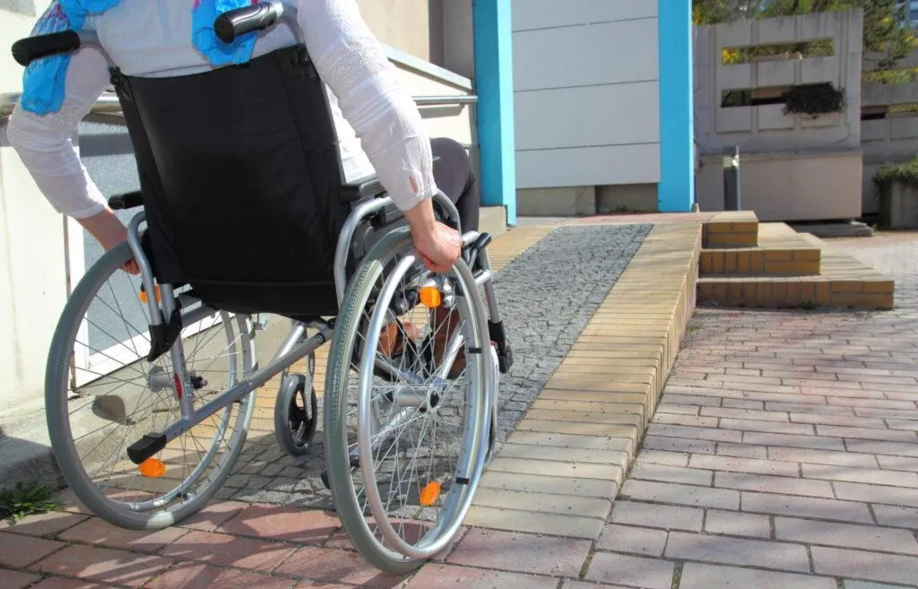 Un homme en fauteuil roulant qui monte une rampe à l'extérieur d'une maison.