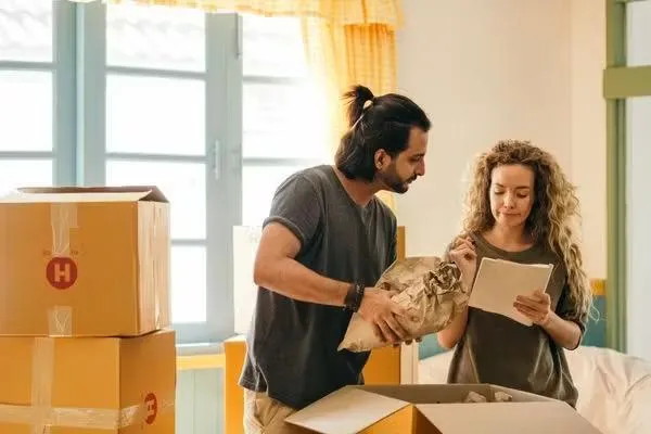 Un couple en plein déménagement, l'homme en plein emballage et la femme qui tient des documents. 