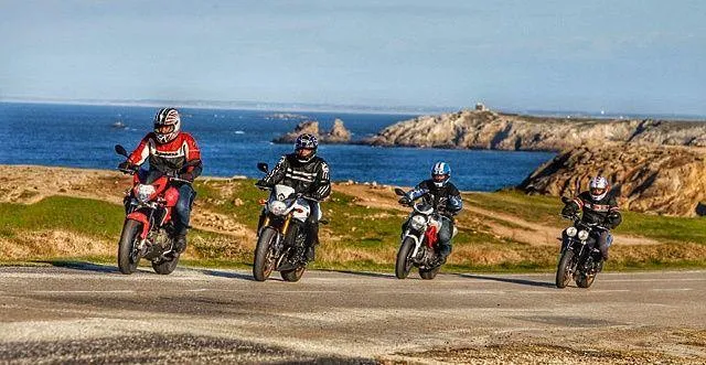 Un groupe de motards qui roule à moto sur une route proche de la mer.