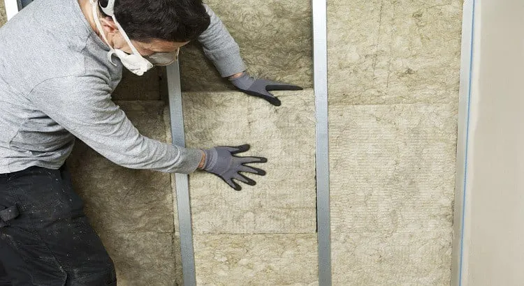 Un homme portant un masque est entrain d'isoler le mur 