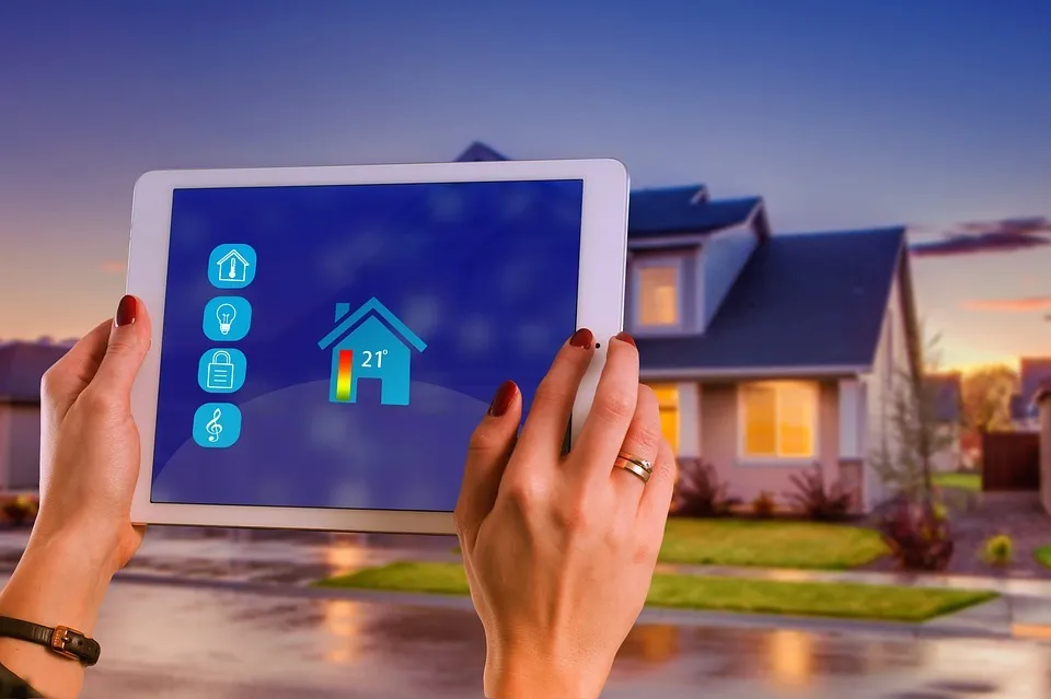 Une main qui tient une tablette connectée à une maison placée dans le fond