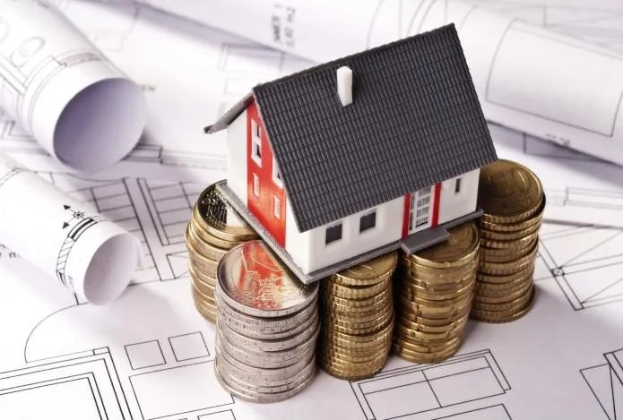 Une maquette de maison posé sur des piles de pièces et des plans de construction