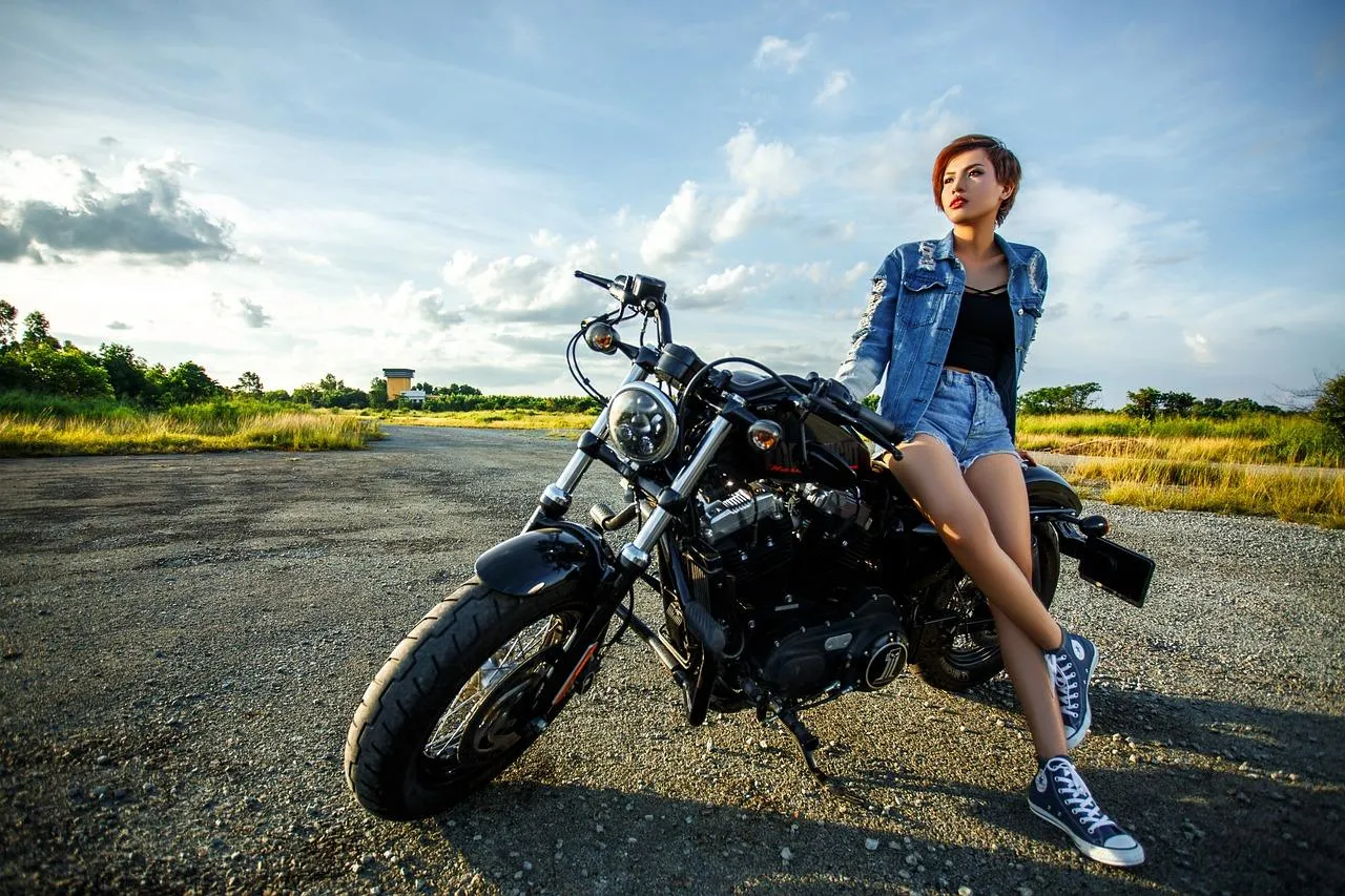 Une femme assise sur une moto garé sur une place entourée de verdure