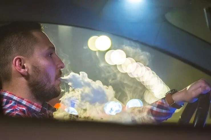Un homme qui produit de la fumée par sa bouche en conduisant