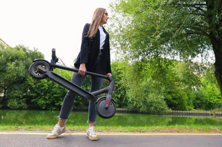 Une femme qui port une trottinette pliée dans sa main