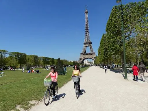 Deux jeunes femmes qui se baladent avec leur vélo à côté de la tour Eiffel.