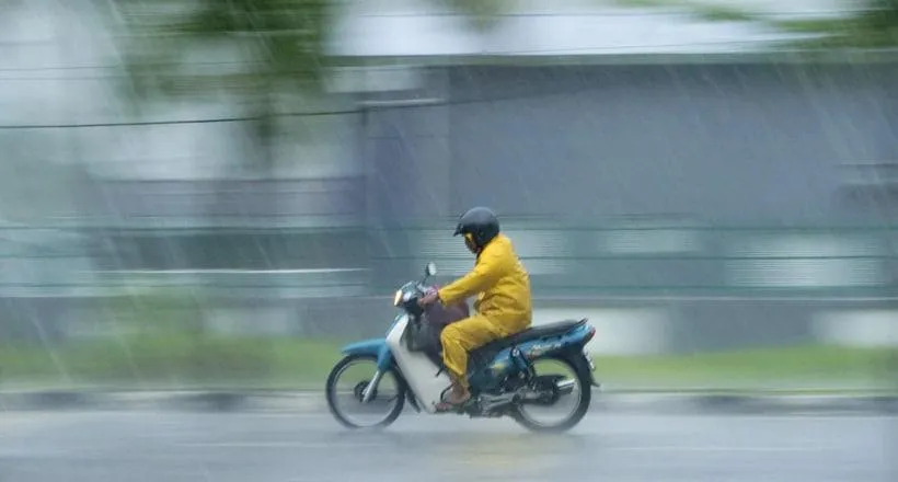 Un homme qui roule sous la pluie à bord de sa moto avec un raglan jaune.