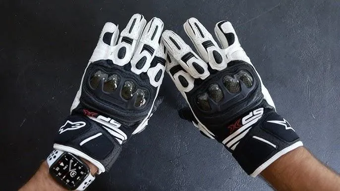 Les gants Alpinestars SP X Air Carbon V2 blanc et noir porté par une main qui les montre sur une table.
