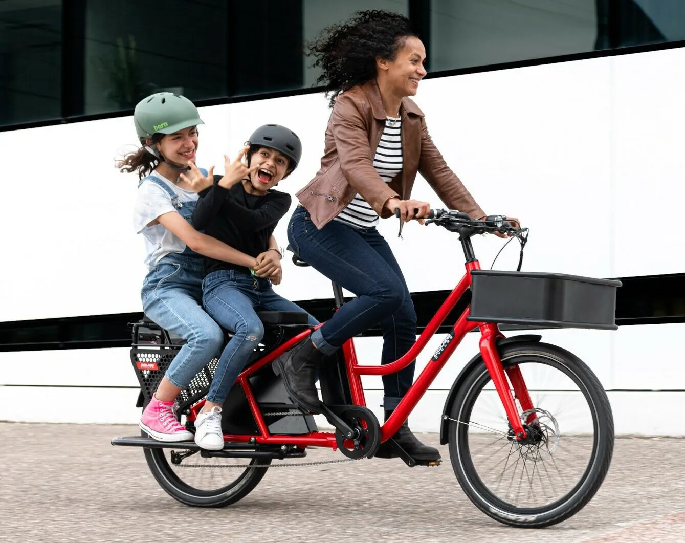 Une femme qui conduit ses enfants sur un vélo longtail rouge