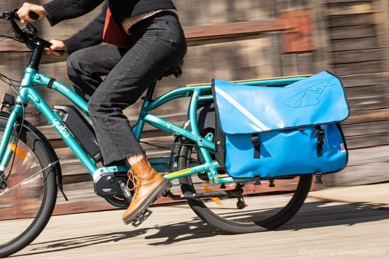 Une femme qui conduit un vélo longtail bleu fluo avec un sacoche bleu à l'arrière