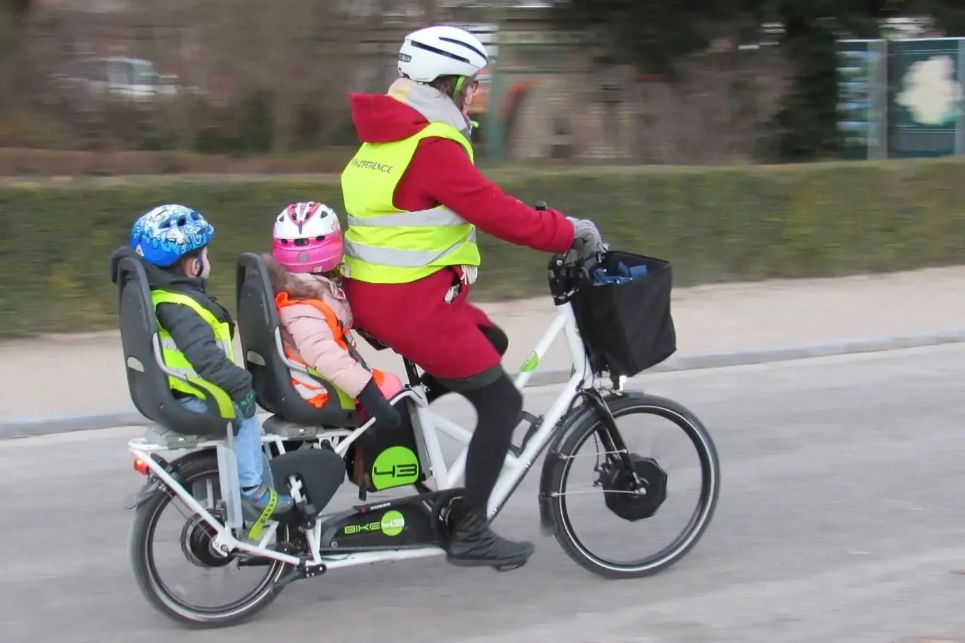 Une femme qui conduit ses deux enfants sur un vélo longtail avec des sièges bébé.