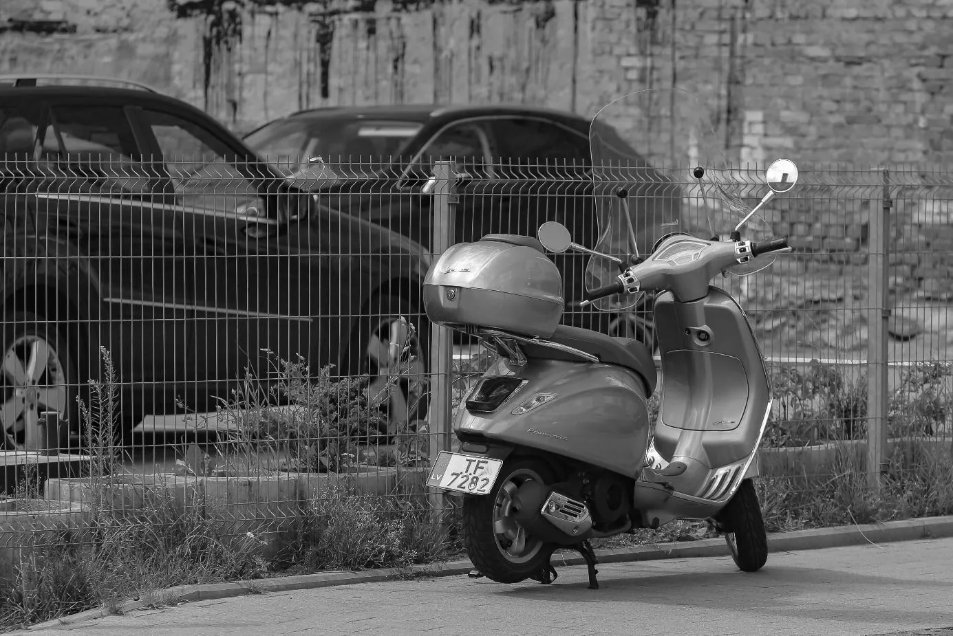 Un scooter garé devant un grillage à côté de quelques voitures garées sur un parking.